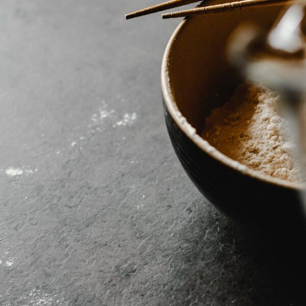 Close-up of a bowl filled with flour and chopsticks on a textured gray surface