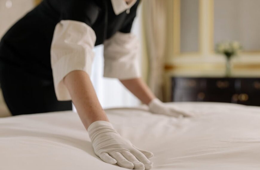 A housekeeper straightening the bed linens in a well-appointed hotel room
