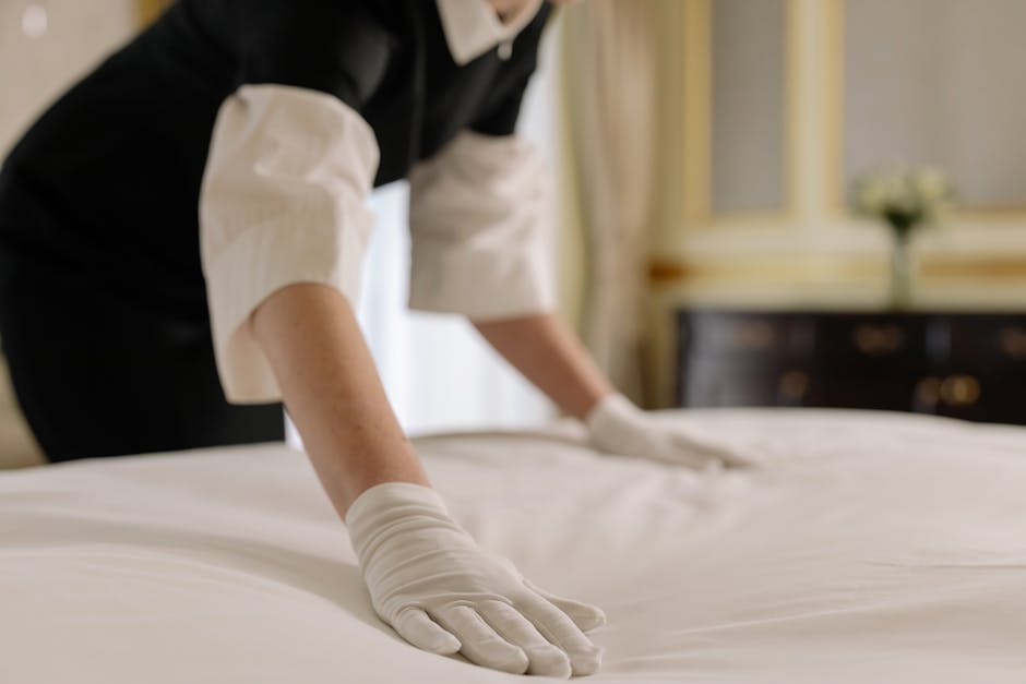 A housekeeper straightening the bed linens in a well-appointed hotel room