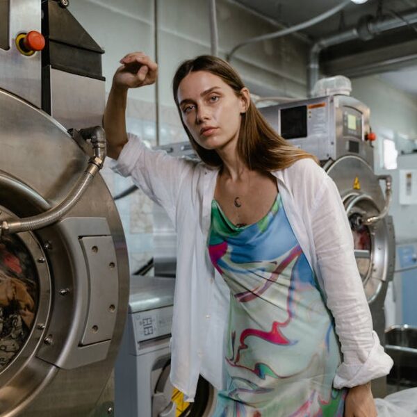 Confident woman in colorful dress posing next to industrial washing machines in a modern laundry facility
