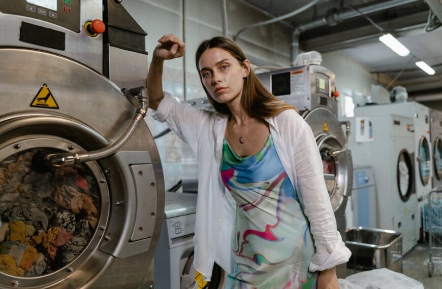 Confident woman in colorful dress posing next to industrial washing machines in a modern laundry facility