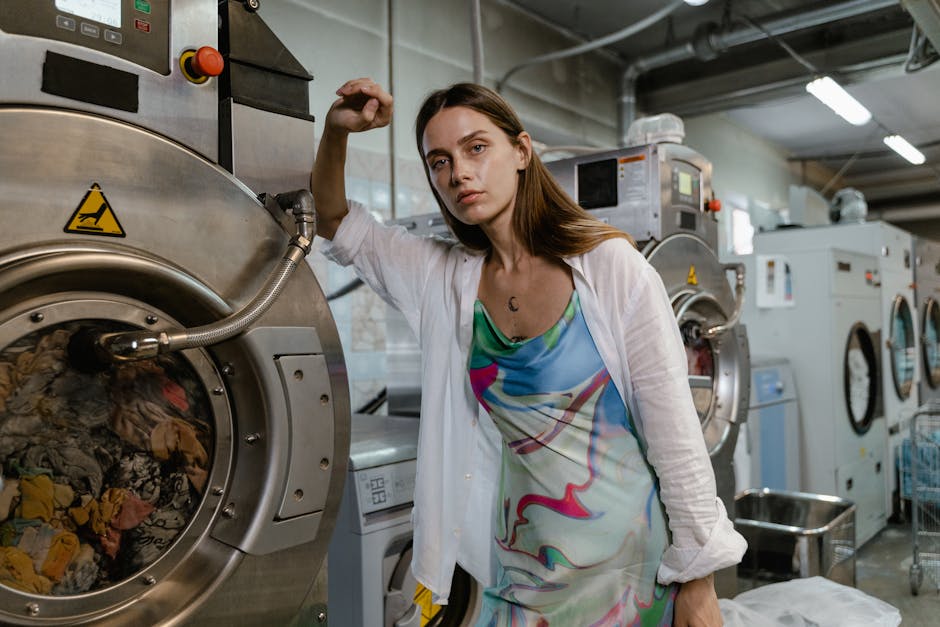 Confident woman in colorful dress posing next to industrial washing machines in a modern laundry facility