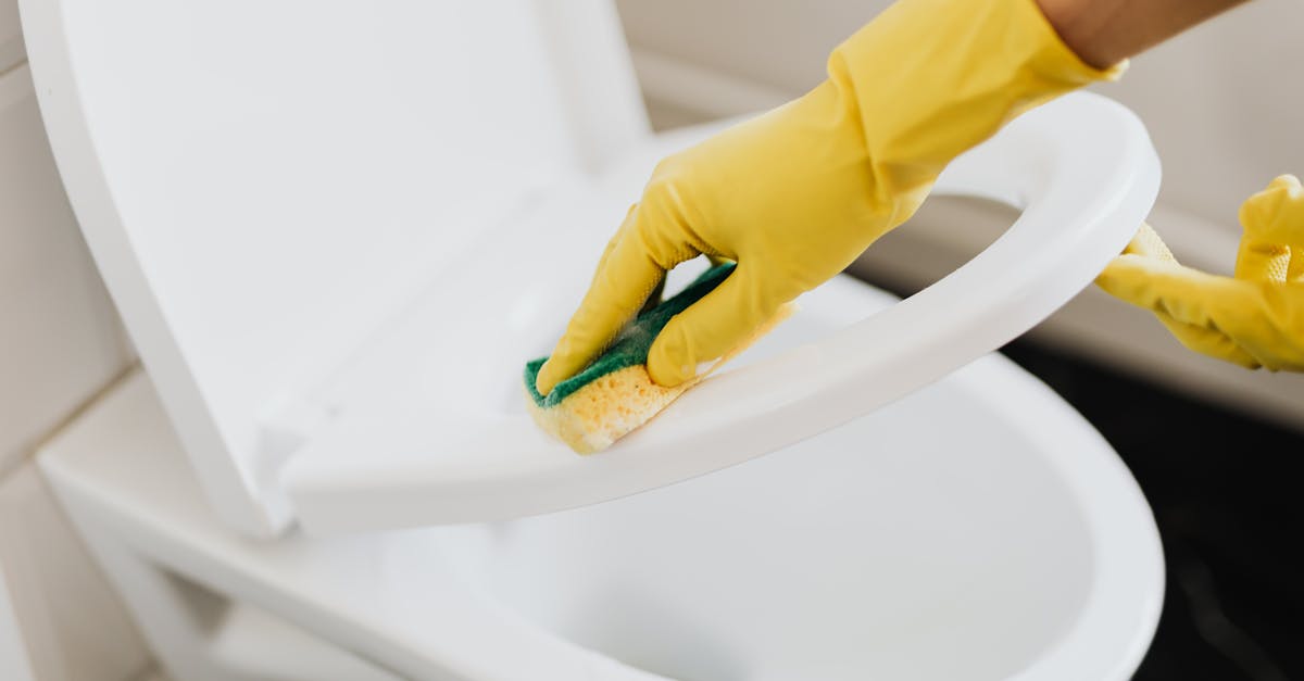 A person using yellow gloves and a sponge to clean a toilet seat indoors