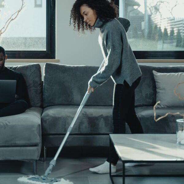 Man working on laptop while woman mops floor in stylish living room