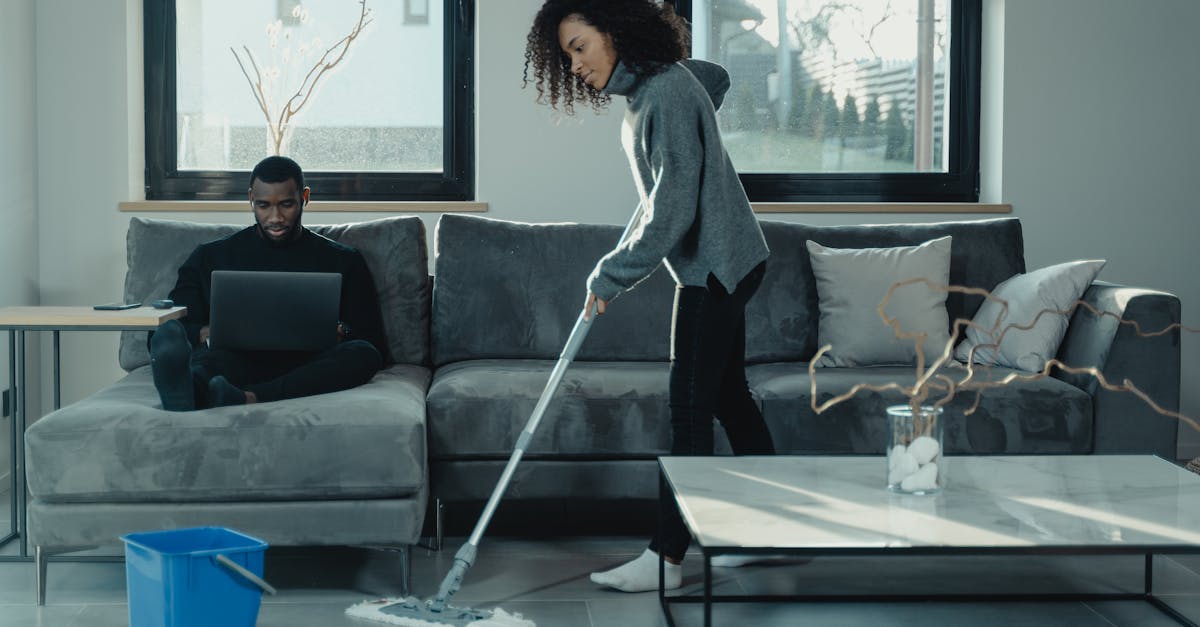 Man working on laptop while woman mops floor in stylish living room