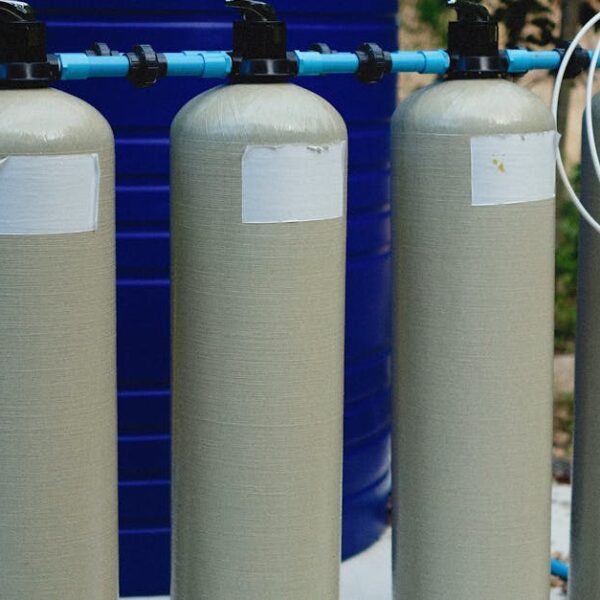 Four beige tanks in an outdoor water treatment setup with blue piping