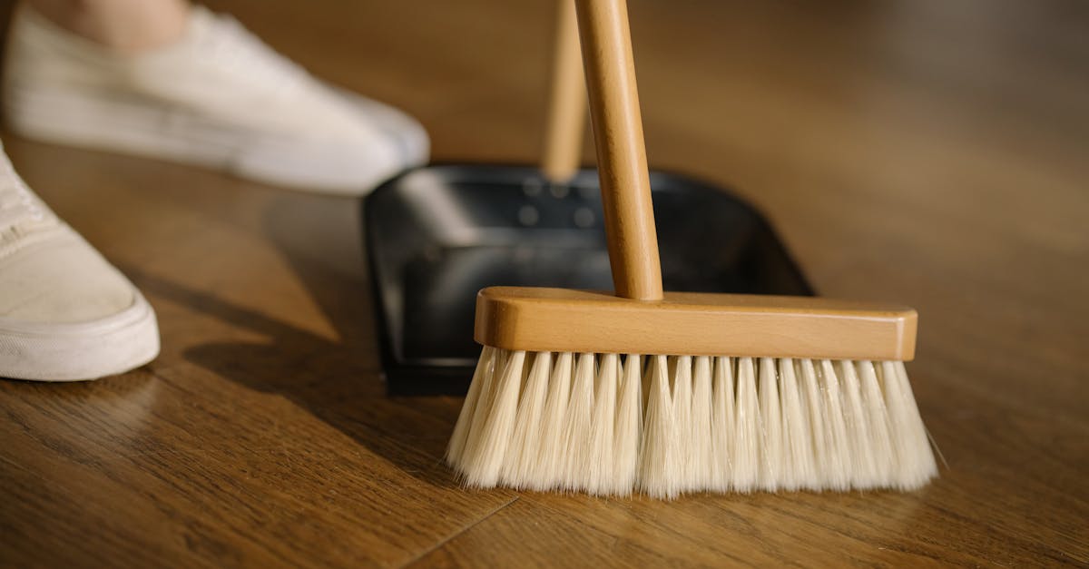 Close-up of a broom and dustpan with white sneakers indoors, representing housekeeping and cleanliness