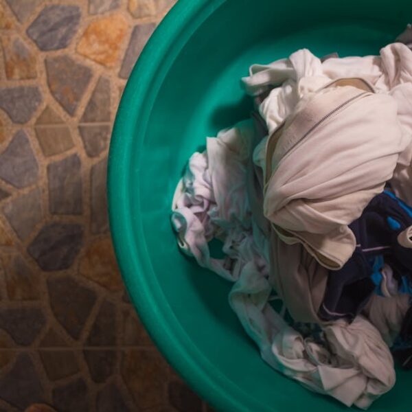 Top view of a laundry basket filled with crumpled clothes on a tiled floor