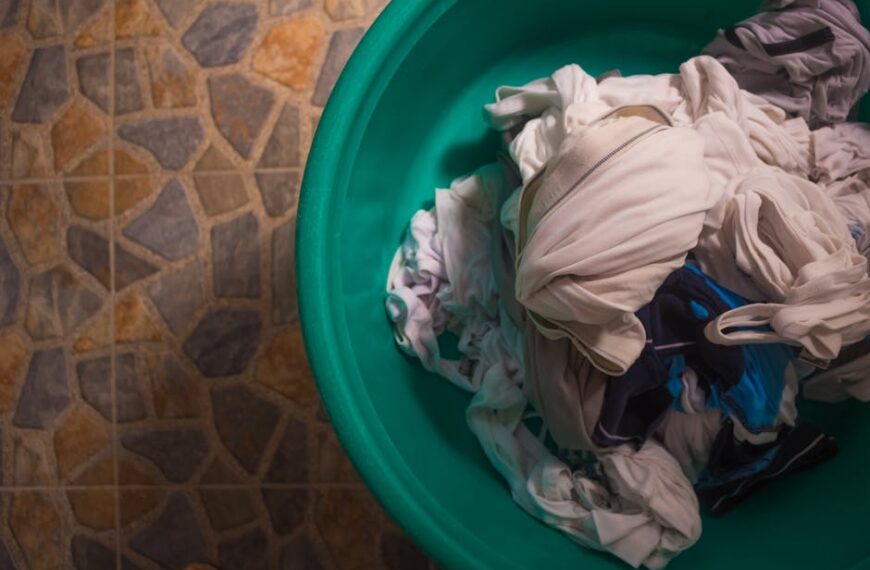 Top view of a laundry basket filled with crumpled clothes on a tiled floor