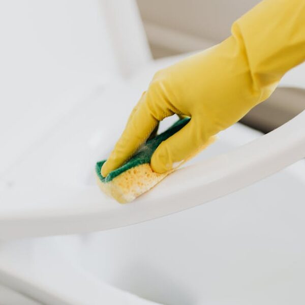 A person using yellow gloves and a sponge to clean a toilet seat indoors